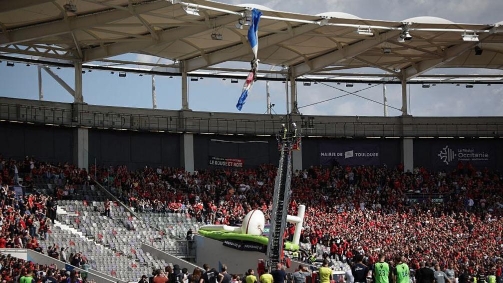 Sale game delayed as parachutist hangs from roof